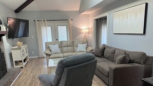 Una sala de estar con un sillón gris, dos sofás, un televisor, una lámpara y una chimenea.