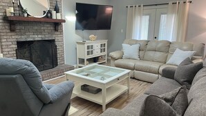 Una sala de estar con chimenea de ladrillo, un televisor de pantalla plana, un sofá beige y una mesa de centro.