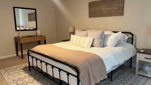 Un dormitorio ordenado con cama, mesitas de noche, un escritorio, un espejo y un ventilador de techo.
