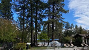 Una piscina con solárium de piedra, rodeada de árboles altos y sillas de descanso.