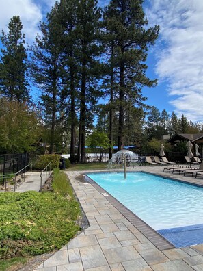 Una piscina con solárium de piedra, rodeada de árboles altos y sillas de descanso.