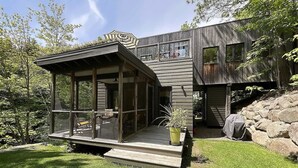 A modern house with a glass-enclosed porch, a deck, and a stone retaining wall.