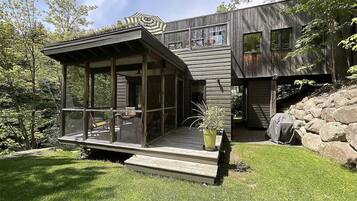 Une maison moderne dotée d’un porche vitré, d’une terrasse et d’un mur de soutènement en pierre.