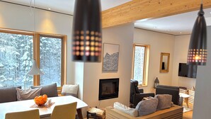 A modern living room with a dining area, large windows, a fireplace, and a television.