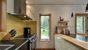 A modern kitchen with a stove, coffee maker, and a window overlooking a garden.