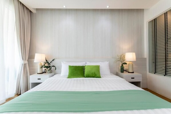 Une chambre à coucher bien rangée, avec un grand lit, deux tables de chevet équipées de lampes et une fenêtre avec des stores.