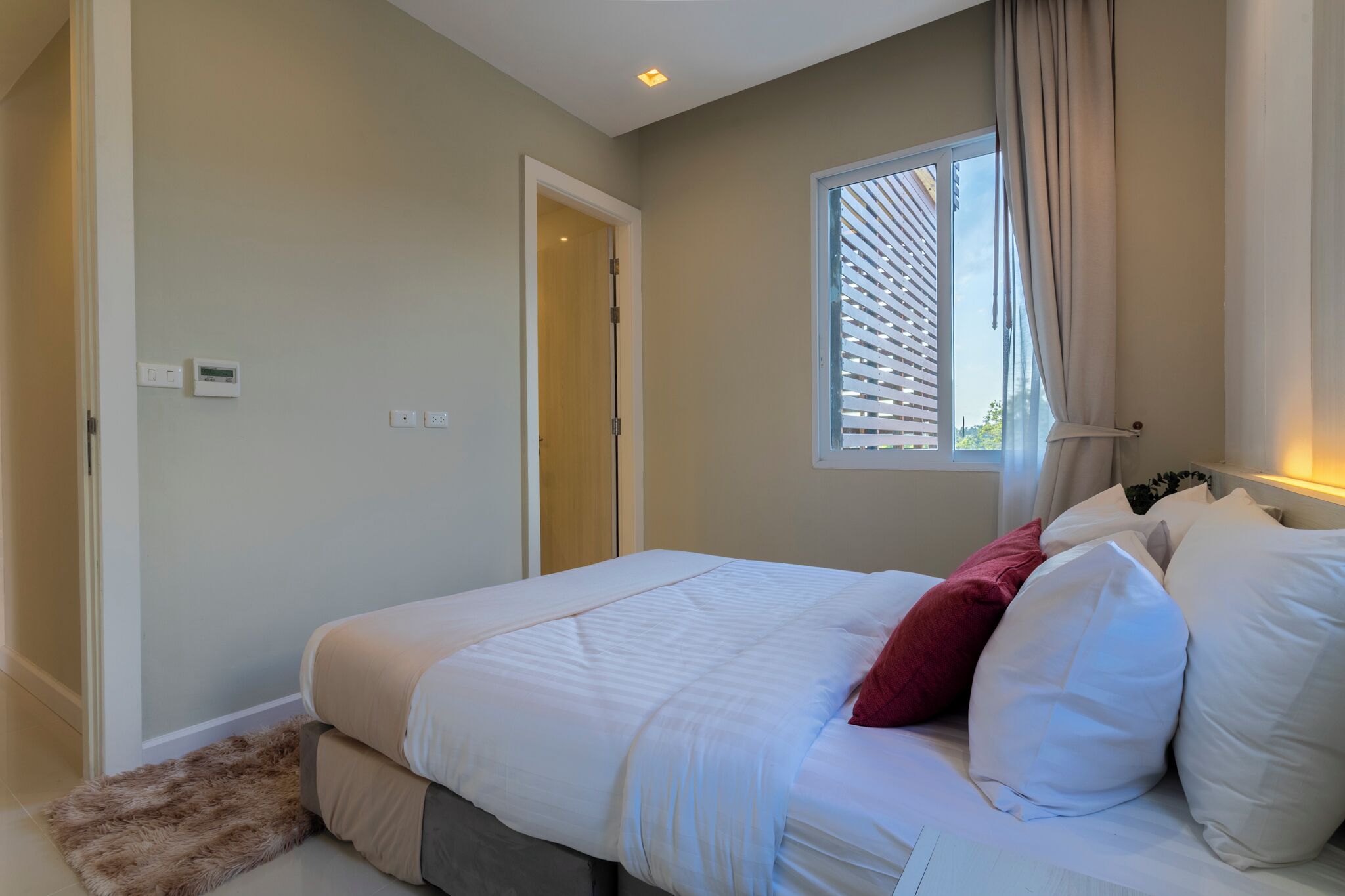 Een slaapkamer met een bed, een raam met zonwering, een deur en een thermostaat aan de muur.