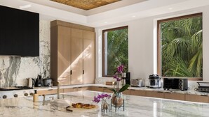 A modern kitchen with a marble countertop, built-in appliances, and large windows offering a view of greenery. - The Luxurious Beach Front Villa Marrakech (Tamarindo)