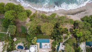 An aerial view of a beachfront property with a swimming pool, lounge area, and dense greenery. - The Luxurious Beach Front Villa Marrakech (Tamarindo)
