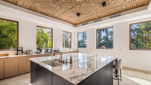 A modern kitchen with a large island, wooden cabinets, and large windows with a view of greenery. - The Luxurious Beach Front Villa Marrakech (Tamarindo)