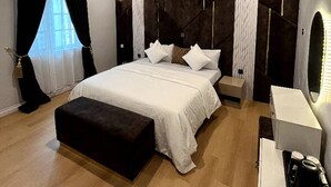 Ett modernt sovrum med en stor säng, sängbord, en bänk och ett skrivbord med en kaffebryggare.