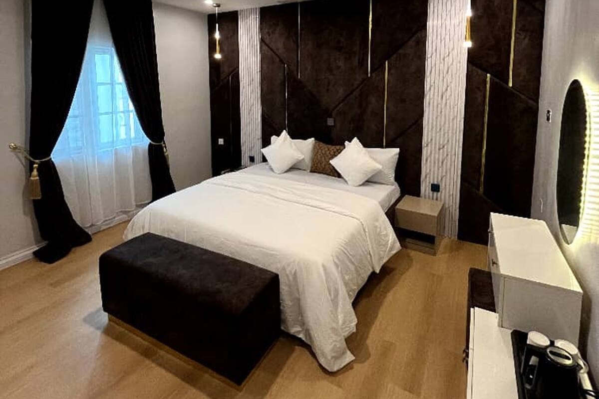 Een moderne slaapkamer met een groot bed, nachtkastjes, een bankje en een bureau met een koffiezetapparaat.