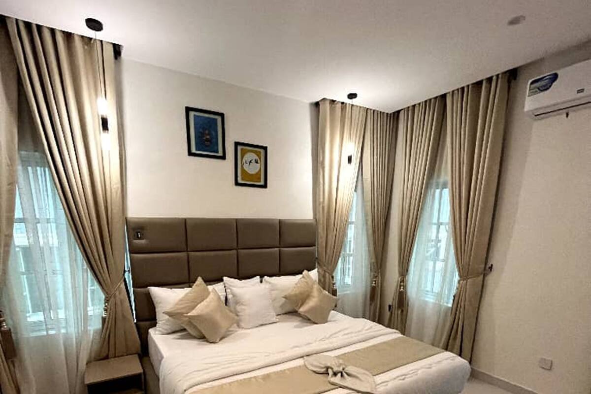 Een moderne slaapkamer met een groot bed, een bankje en gordijnen.