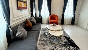Ett modernt vardagsrum med en grå soffa, en orange fåtölj, ett runt soffbord och en mönstrad matta.