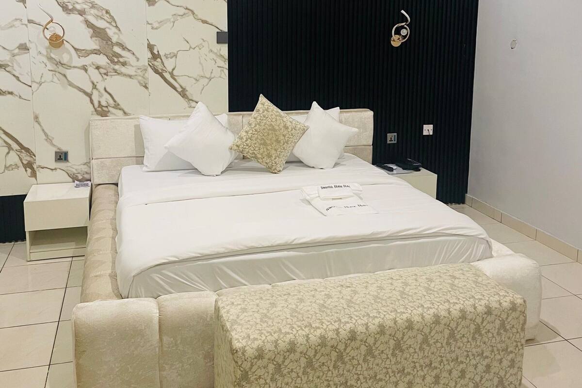 Een moderne slaapkamer met een groot bed, een nachtkastje, een bankje en een donkere accentmuur.