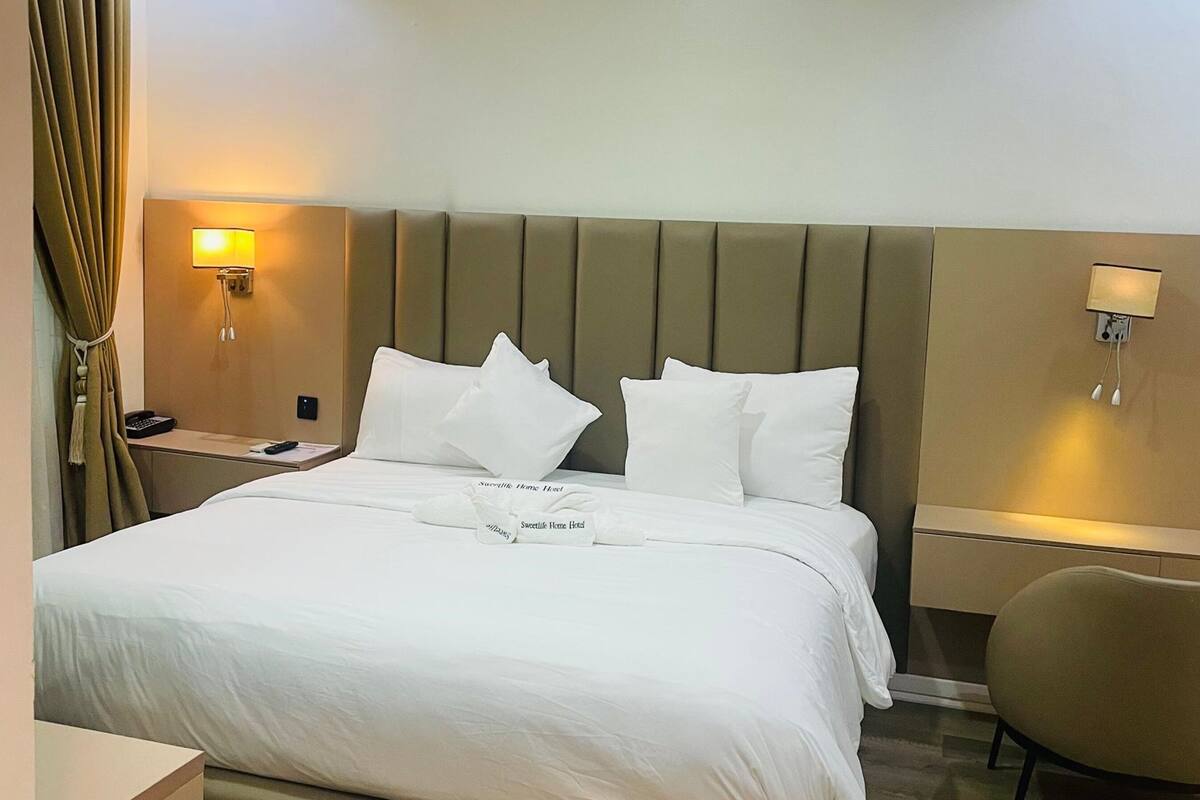Een moderne hotelkamer met een groot bed, een nachtkastje, een stoel en een hoofdbord met ingebouwde verlichting.