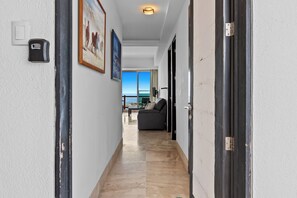 Un pasillo con una puerta a la derecha, un cuadro a la izquierda y, al fondo, vistas a un balcón con una mesa y sillas.