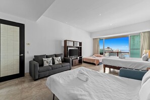 Habitación de hotel moderna con una cama grande, un sofá, un televisor y un balcón con vistas al mar.