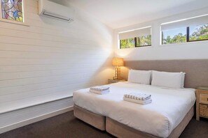 Une chambre d’hôtel avec un grand lit, une table de chevet avec une lampe, une fenêtre donnant sur un paysage verdoyant et un vitrail sur le mur.
