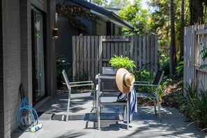 Un espace patio avec des sièges d’extérieur, une raquette de tennis et un chapeau posé sur une chaise.