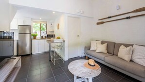 Un espace de vie compact comprenant un coin cuisine, un canapé et une table ronde surmontée d’un abat-jour.