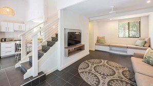 Een moderne woonkamer met een trap, een flatscreen-tv, een bank en een vloerkleed met een patroon.