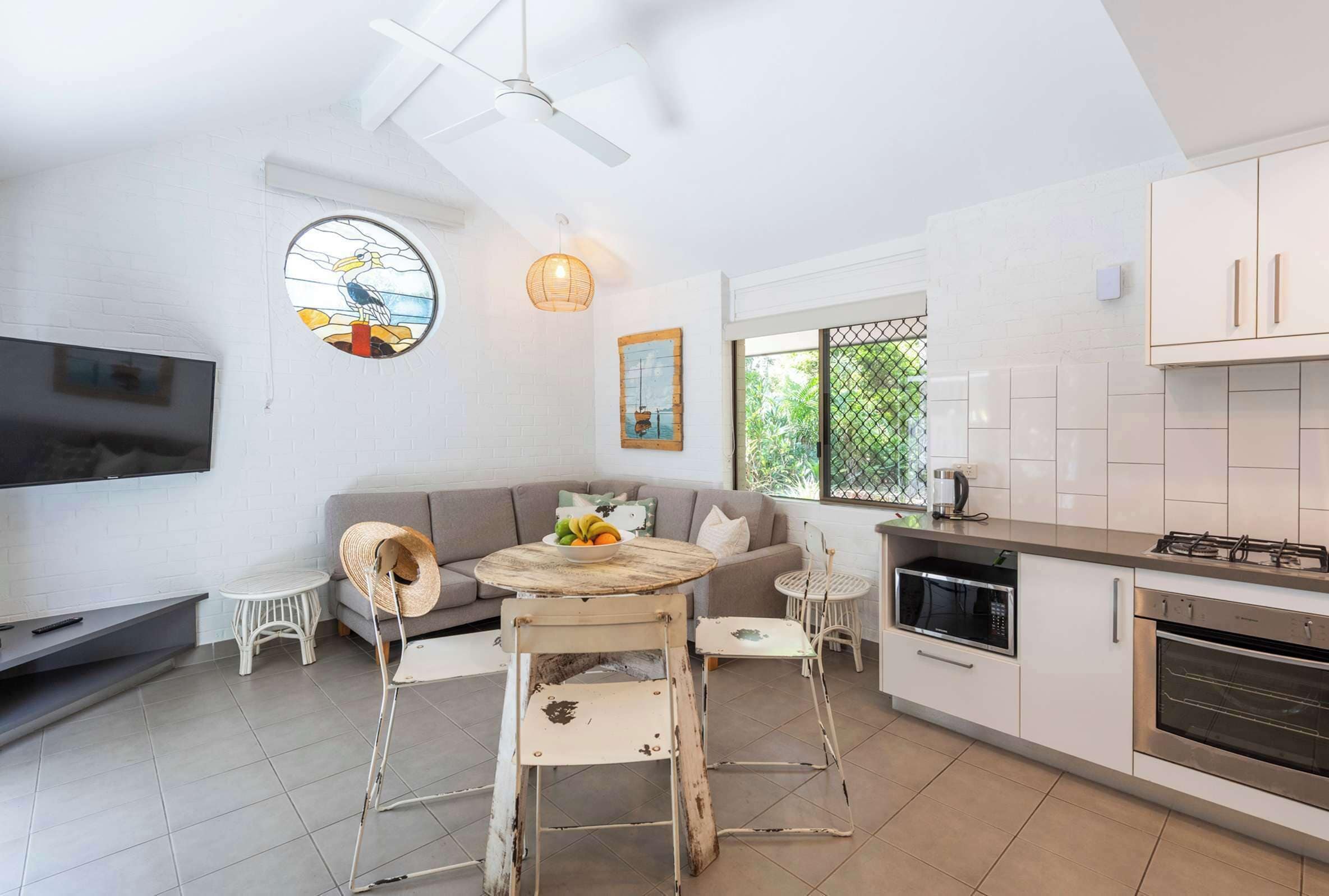 A modern kitchen with white cabinets, a built-in oven, and a dining area with a round table and chairs.