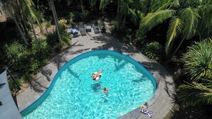 A swimming pool surrounded by palm trees and a lounge area with chairs.