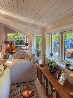 A modern living room with a sofa, a lamp, a coffee table, and a view of greenery outside. - Holiday oasis with terrace and sloping garden (Tikøb)