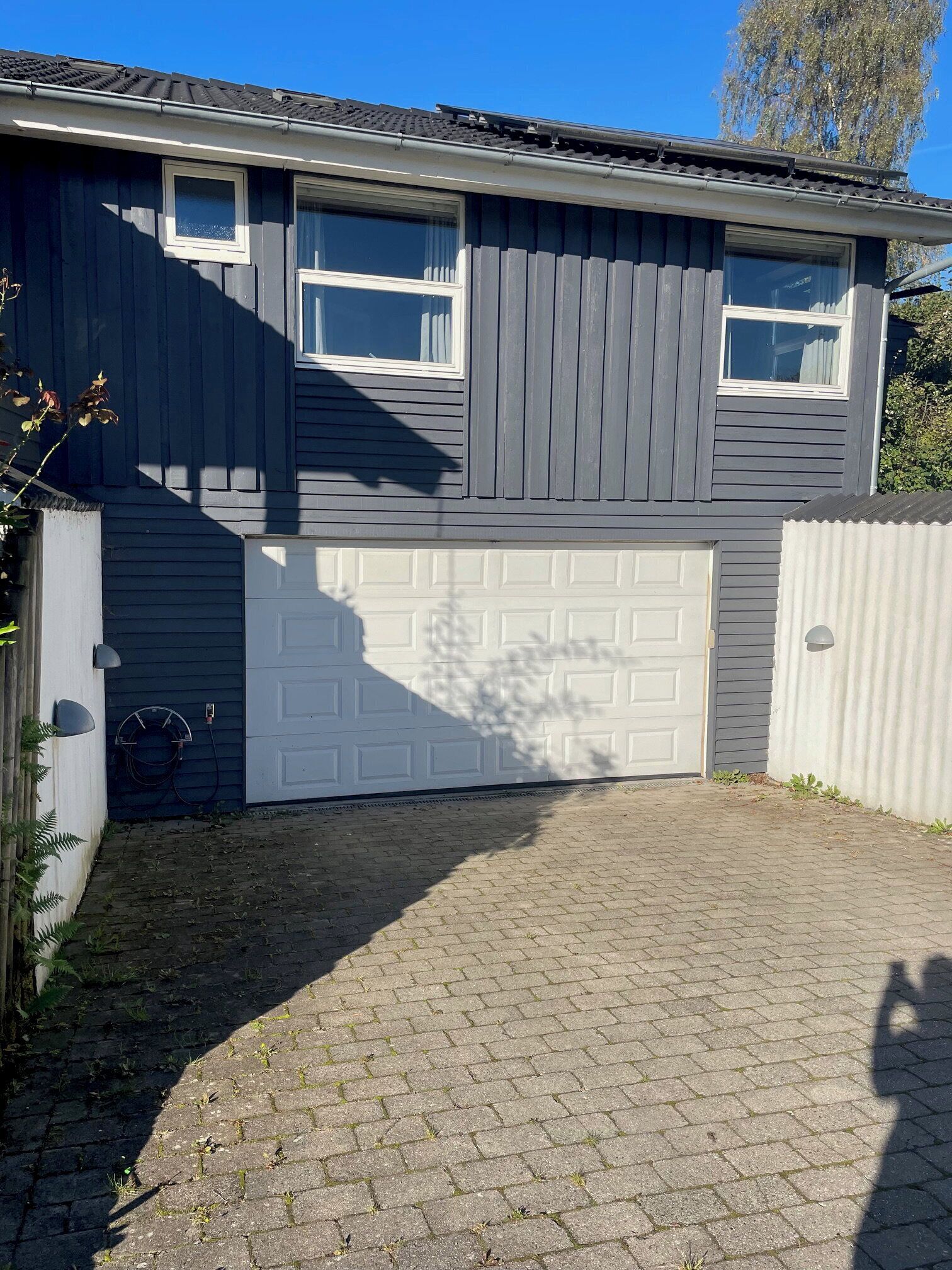 Uma casa de dois andares com garagem, entrada de tijolos e uma árvore ao fundo.