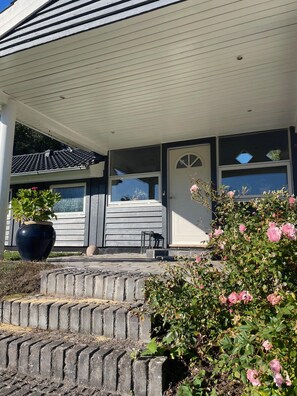 A house with a covered porch, a large potted plant, and a rose bush. - Holiday oasis with terrace and sloping garden (Tikøb)