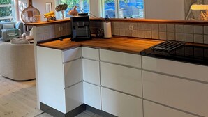 A modern kitchen with a wooden countertop, white cabinetry, and pendant lighting. - Holiday oasis with terrace and sloping garden (Tikøb)