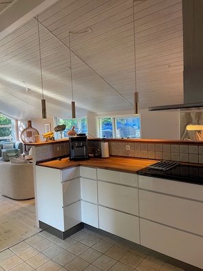 A modern kitchen with a wooden countertop, white cabinetry, and pendant lighting. - Holiday oasis with terrace and sloping garden (Tikøb)