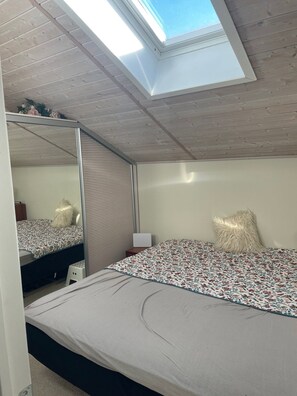 A bedroom with a skylight, a bed with a floral bedspread, a bedside table, and a mirror. - Holiday oasis with terrace and sloping garden (Tikøb)