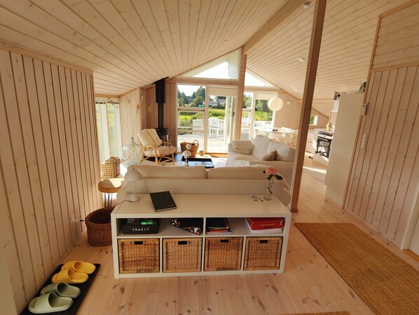A cozy interior with a sofa, a fireplace, wicker baskets, and a view of the outdoors. - Quiet cottage near nature water and views (Rude)