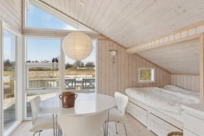 A room with a loft bed, a dining table with chairs, a hanging light fixture, and large windows offering a view of the outdoors. - Quiet cottage near nature water and views (Rude)