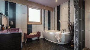 A modern bathroom with a large bathtub, a vanity with a mirror, and a window.