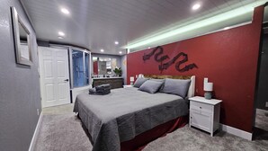 A modern bedroom with a large bed, a walk-in closet, a bathroom with a shower, and a red accent wall. - 1 Bedroom Luxurious Loft perfect for Entertaining! (Colorado Springs)