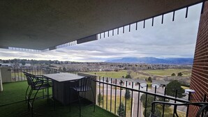 A balcony with a table and chairs, a view of a town and mountains, and a brick wall. - 1 Bedroom Luxurious Loft perfect for Entertaining! (Colorado Springs)
