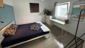 Een slaapkamer met een bed, een bureau, een raam en een potplant.