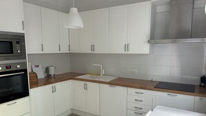 Een moderne keuken met witte kastjes, een houten aanrecht, een ingebouwde oven, een koffiezetapparaat en een hangende hanglamp.