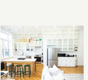 A modern kitchen with white cabinetry, a stainless steel refrigerator, and a dining area with a wooden table and green stools.