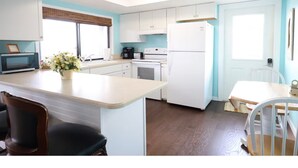 Cozinha compacta com armários brancos, geladeira, micro-ondas e área de refeições com mesa e cadeiras.