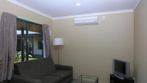 Una sala de estar con un sofá, una mesa de centro de vidrio, un televisor sobre un mueble bajo y un equipo de aire acondicionado en la pared.