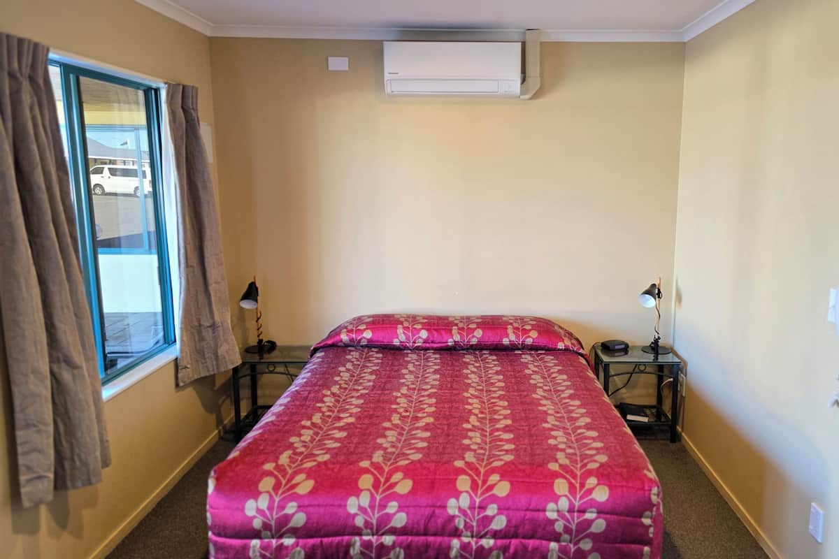 Habitación de hotel con cama, dos mesitas de noche, ventana con cortinas, equipo de aire acondicionado y teléfono instalado en la pared.
