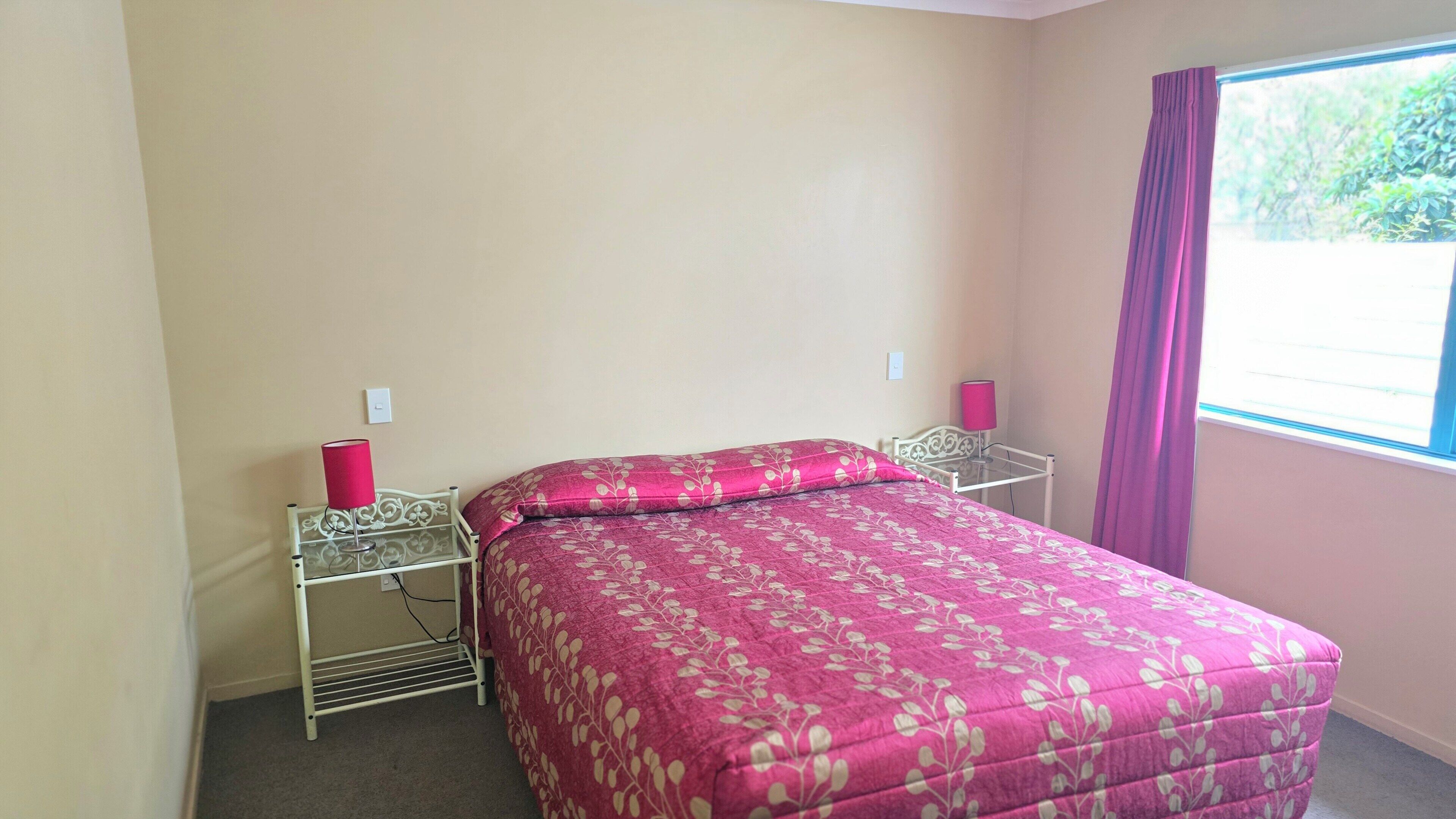 A single bed with a floral bedspread, two bedside tables with lamps, a window with curtains, and a light switch on the wall.