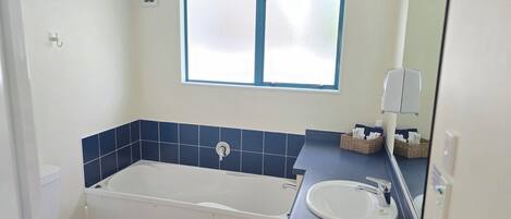 A bathroom with a bathtub, a sink, a window, and a mirror.