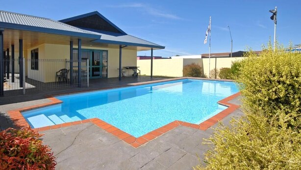 Una piscina con borde azul, un porche cubierto y un edificio con techo azul.