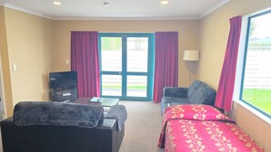 Habitación de hotel con cama, sofá, escritorio con televisor y ventana con cortinas.