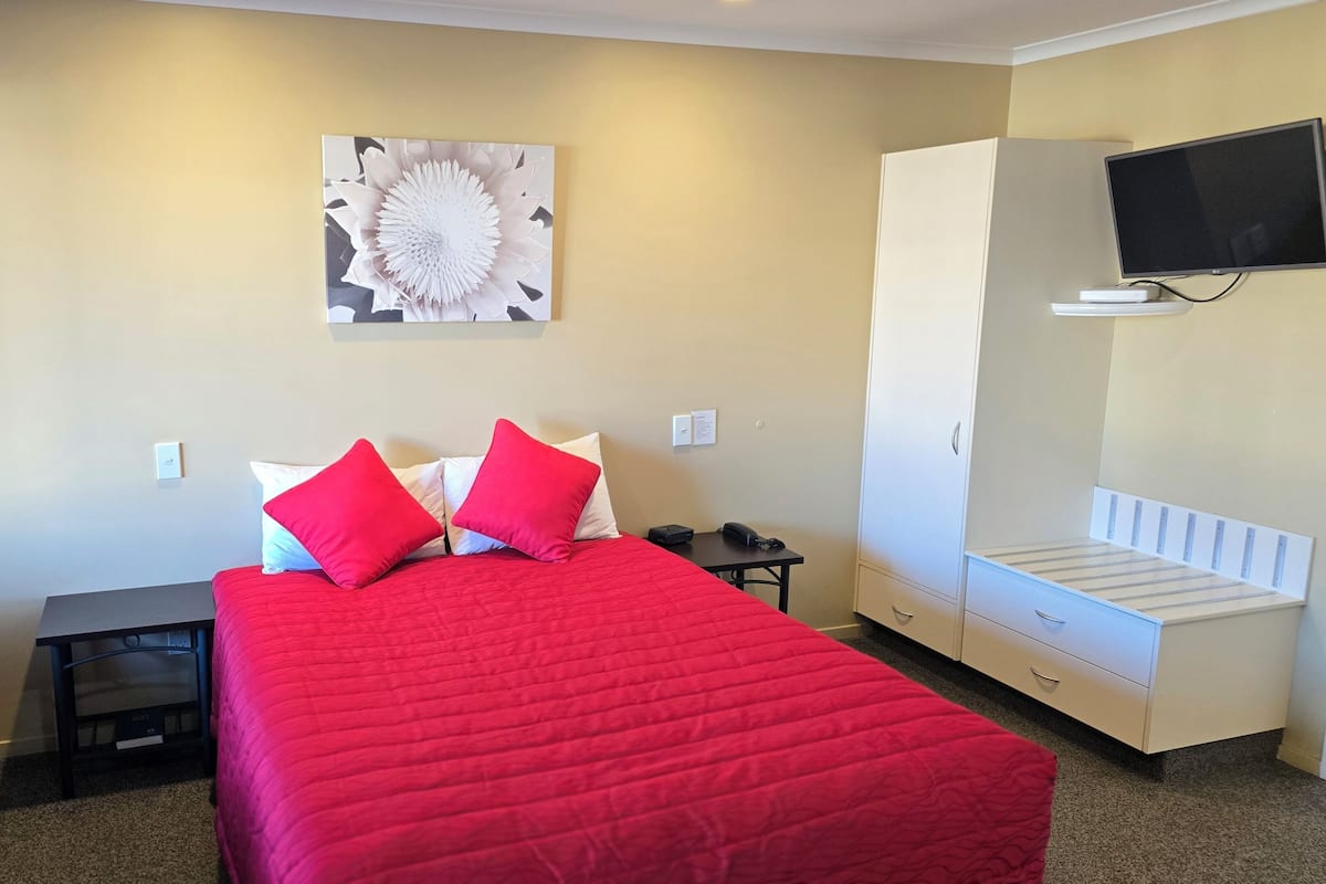 Una habitación de hotel con cama, escritorio, silla, televisor y armario.
